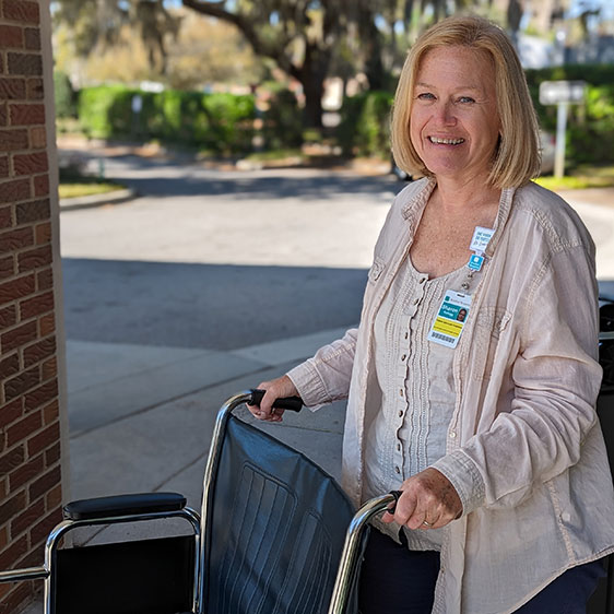  ED Ambassador Sharon Kellogg stands behind a wheelchair and smiles at the camera