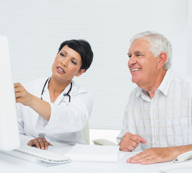 A female physician and male patient review information on a computer screen.