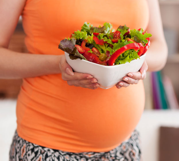 A pregnant woman pictured from the neck down holding a salad