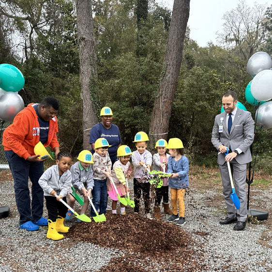 A group of children hold shovels and pick up mulch