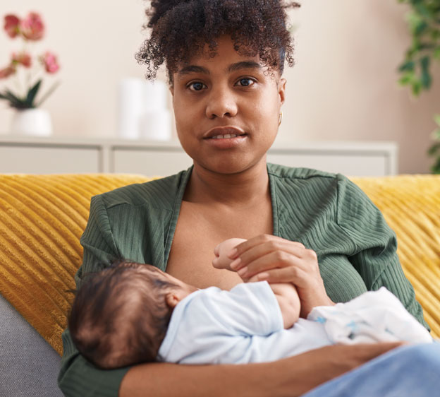 A mother breastfeeding a baby and looking toward the camera