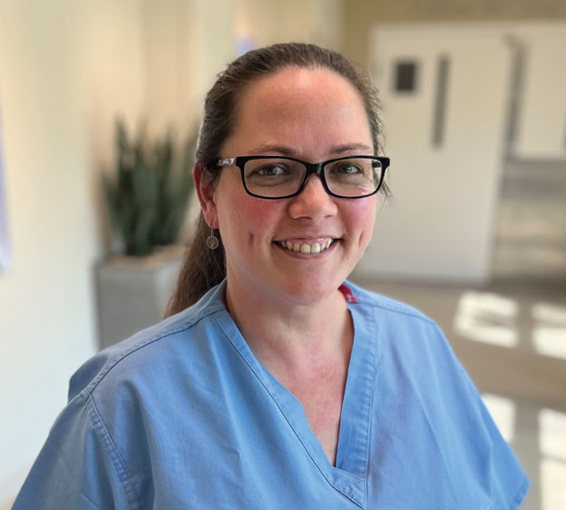 A photograph of a nurse named Beth Montana in blue scrubs smiling for the camera
