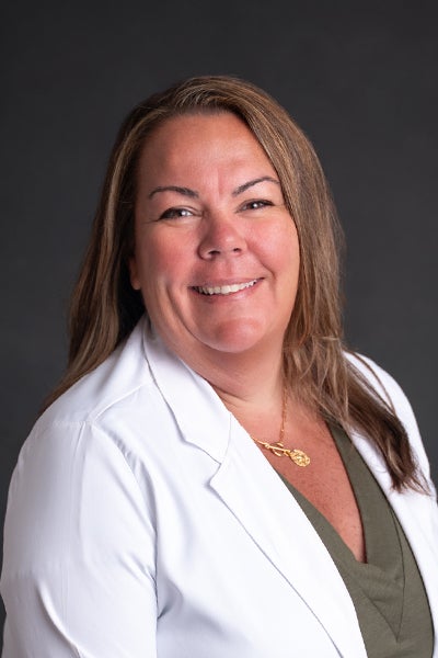 Professional headshot of Amy Morrissette wearing an olive green shirt and a white lab coat over it in front of a dark gray backdrop.