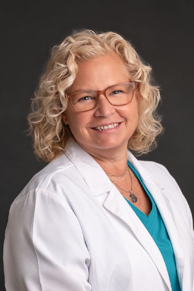 Kim Wade, an oncology nurse navigator at Beaufort Memorial, wearing teal blue scrubs and a white lab coat in front of a dark grey backdrop.